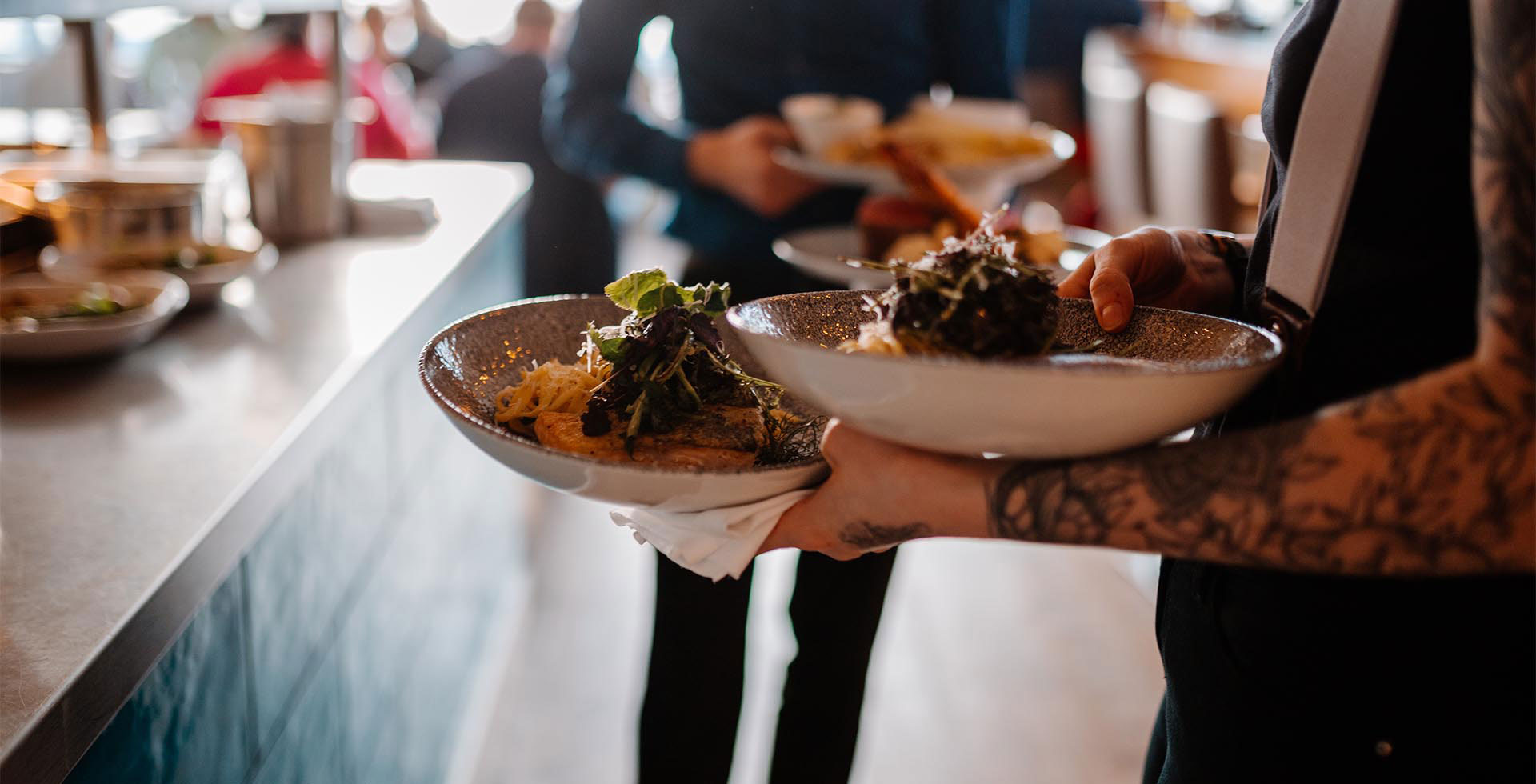 Servicekraft trägt mehrere angerichtete Teller durch den Restaurantbereich des THE GRAND Ahrenshoop.