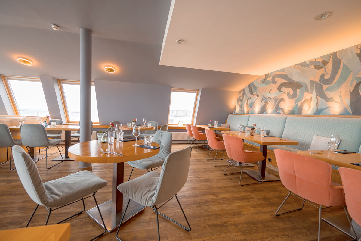 Restaurant im THE GRAND Ahrenshoop mit gedeckten Tischen, warmem Licht und Blick Richtung Ostsee.
