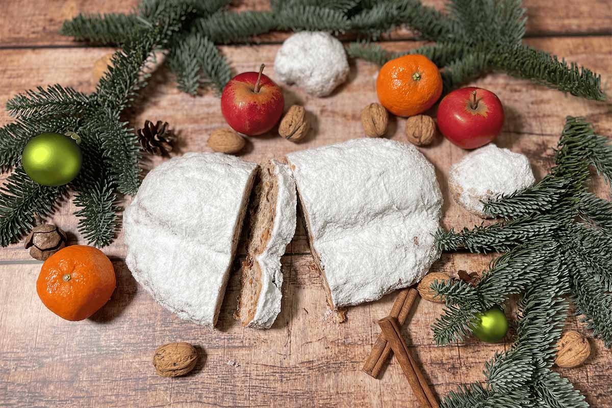 Angeschnittener Stollen liegt zwischen Tannenzweigen, Äpfeln, Mandarinen und Nüssen auf einem Holztisch in Ahrenshoop.