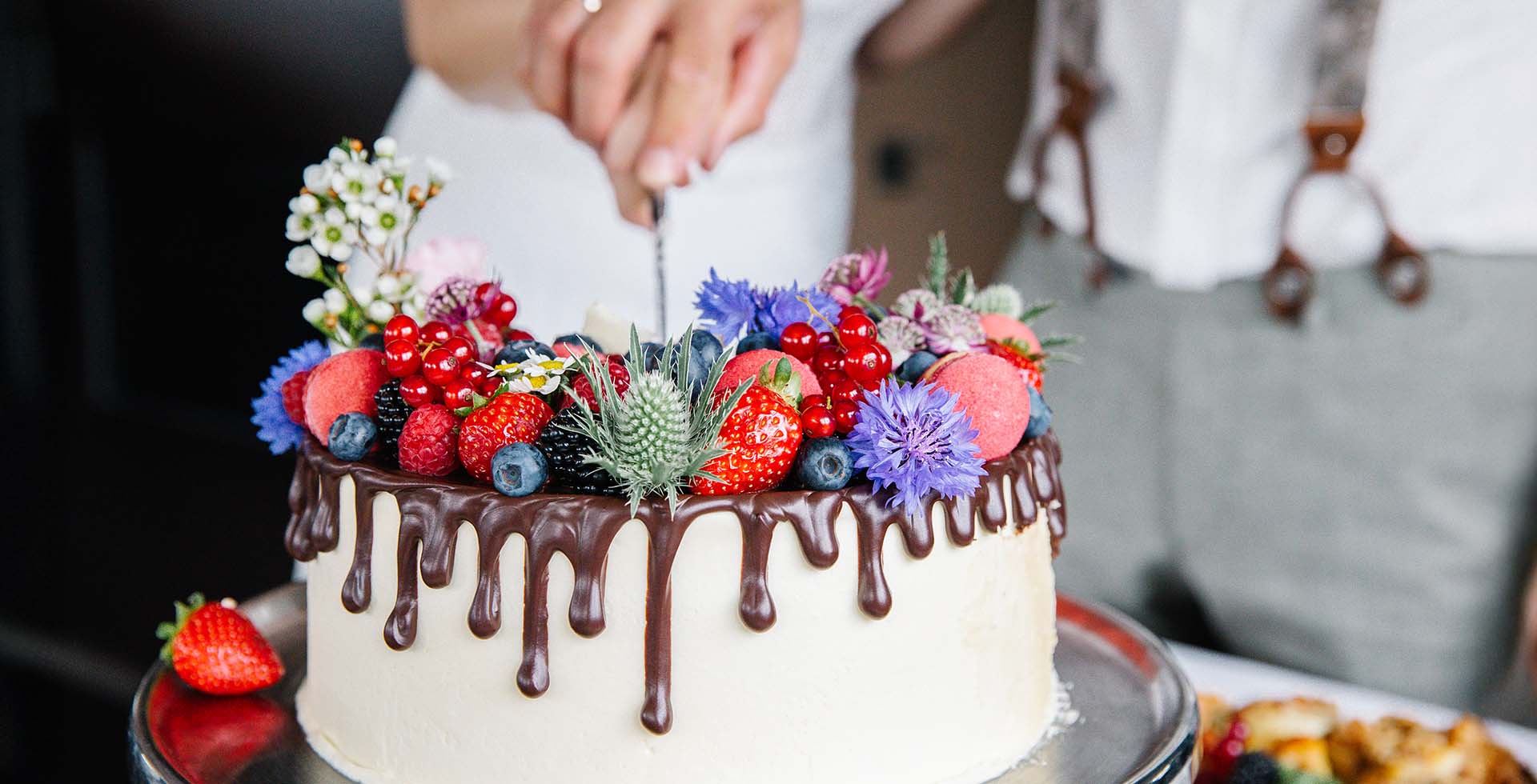 Torte mit Beeren, Blumen und Schokoladenguss wird bei einer Feier in Ahrenshoop angeschnitten.