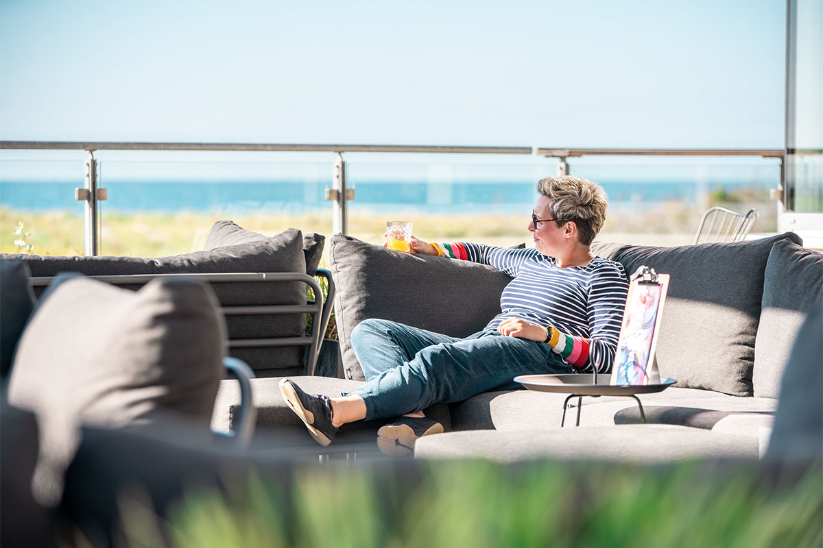 Frau sitzt entspannt auf einer Terrasse mit Ostseeblick im SEASIDE Restaurant.