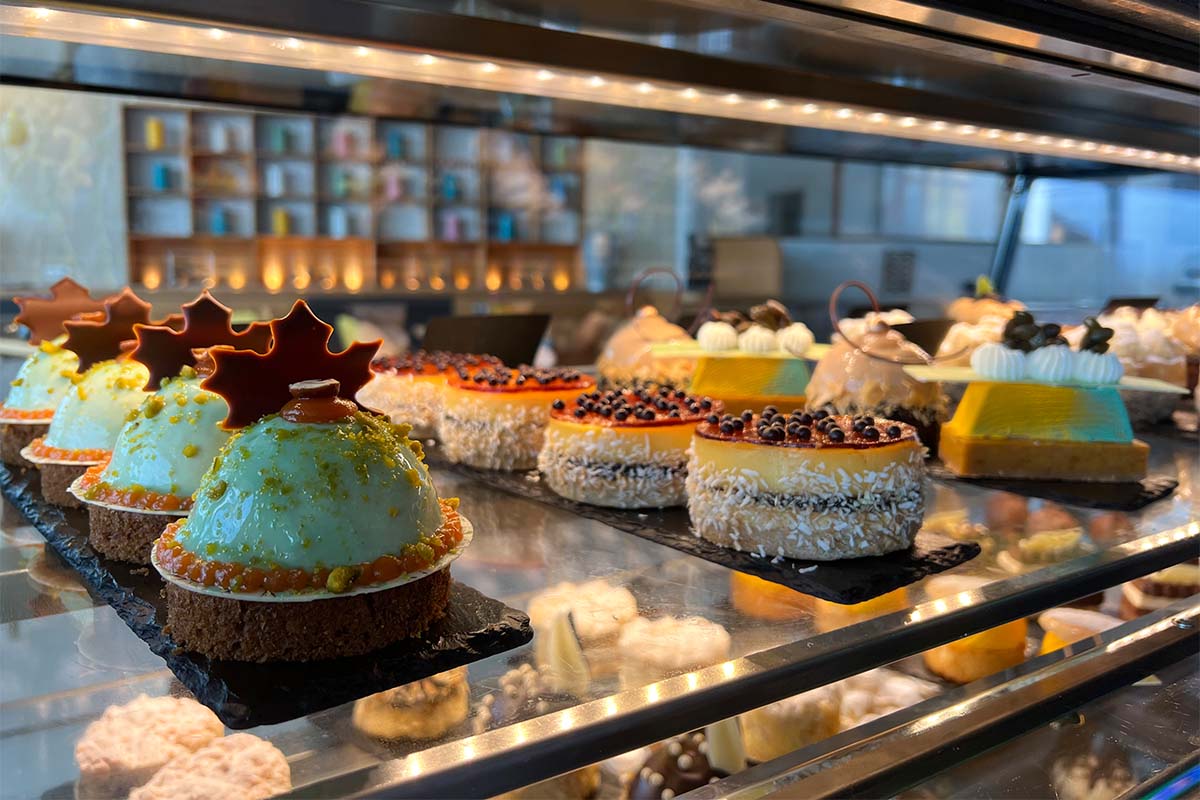 Kunstvoll dekorierte Törtchen stehen in einer beleuchteten Vitrine der Patisserie THE GRAND Ahrenshoop.