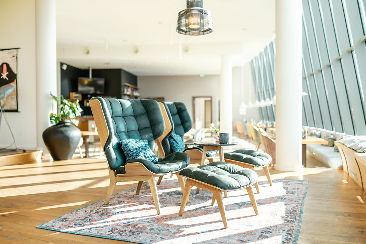 Gemütliche Sessel mit Hocker stehen im THE GRAND Ahrenshoop mit großer Fensterfront an der Ostsee.