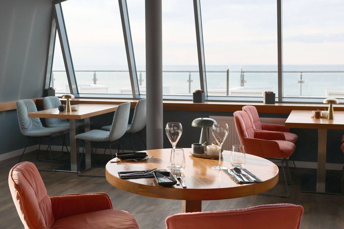 Modernes Restaurant WEITBLICK mit runden Tischen und Ostseeblick durch große Fensterfront.