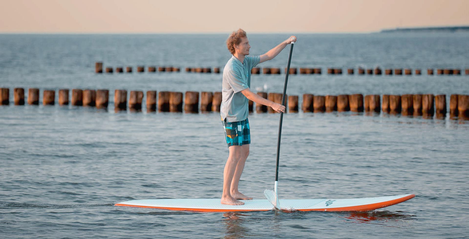 Mann steht auf einem Stand-up-Paddle-Board und paddelt auf ruhiger Ostsee vor Ahrenshoop.