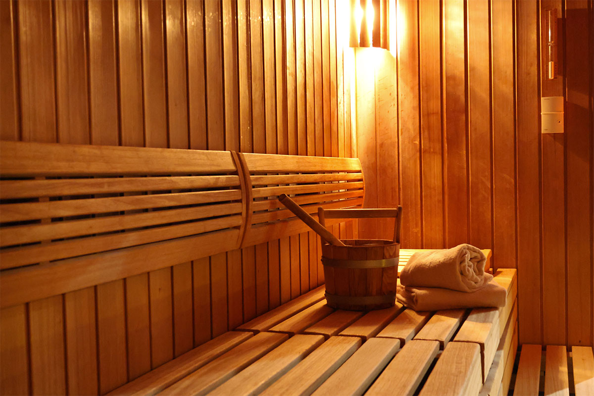Holzsauna mit Bank, Aufgusseimer und zusammengerolltem Handtuch im Wellnessbereich des THE GRAND Ahrenshoop.